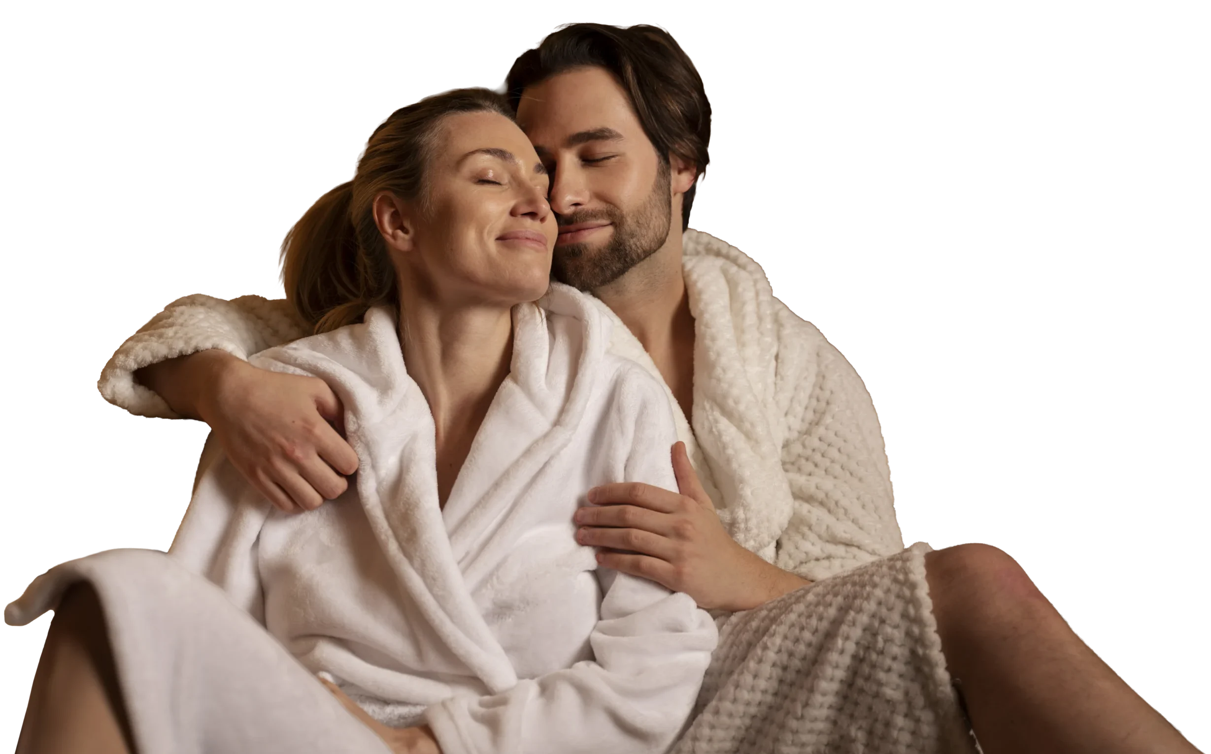 Un couple vêtu d'un peignoir blanc est assis l'un contre l'autre, souriant paisiblement, les yeux fermés, profitant d'un moment de détente et d'affection.